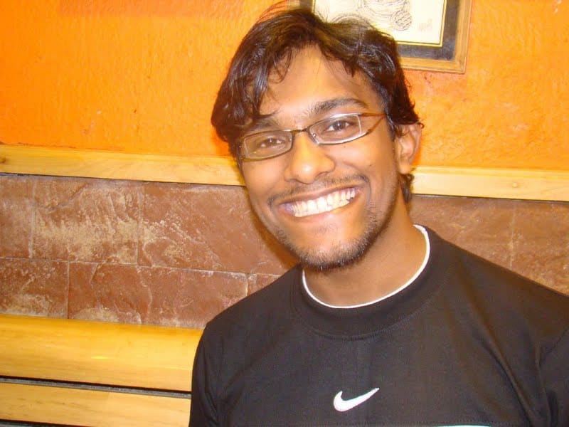 "The author in 2009, smiling, in glasses and a black T-shirt against an orange wall."
